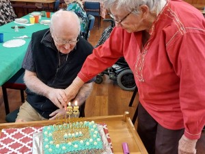 Two people cutting a green, white and gold iced rectangular cake.  
